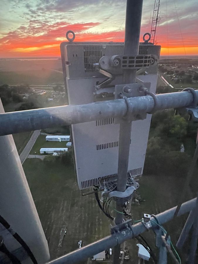 Sunset behind a radio on a tower antenna mount, a town far below