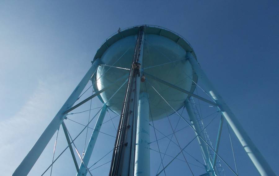 Looking up at a water tank with a climber on the cable ladder